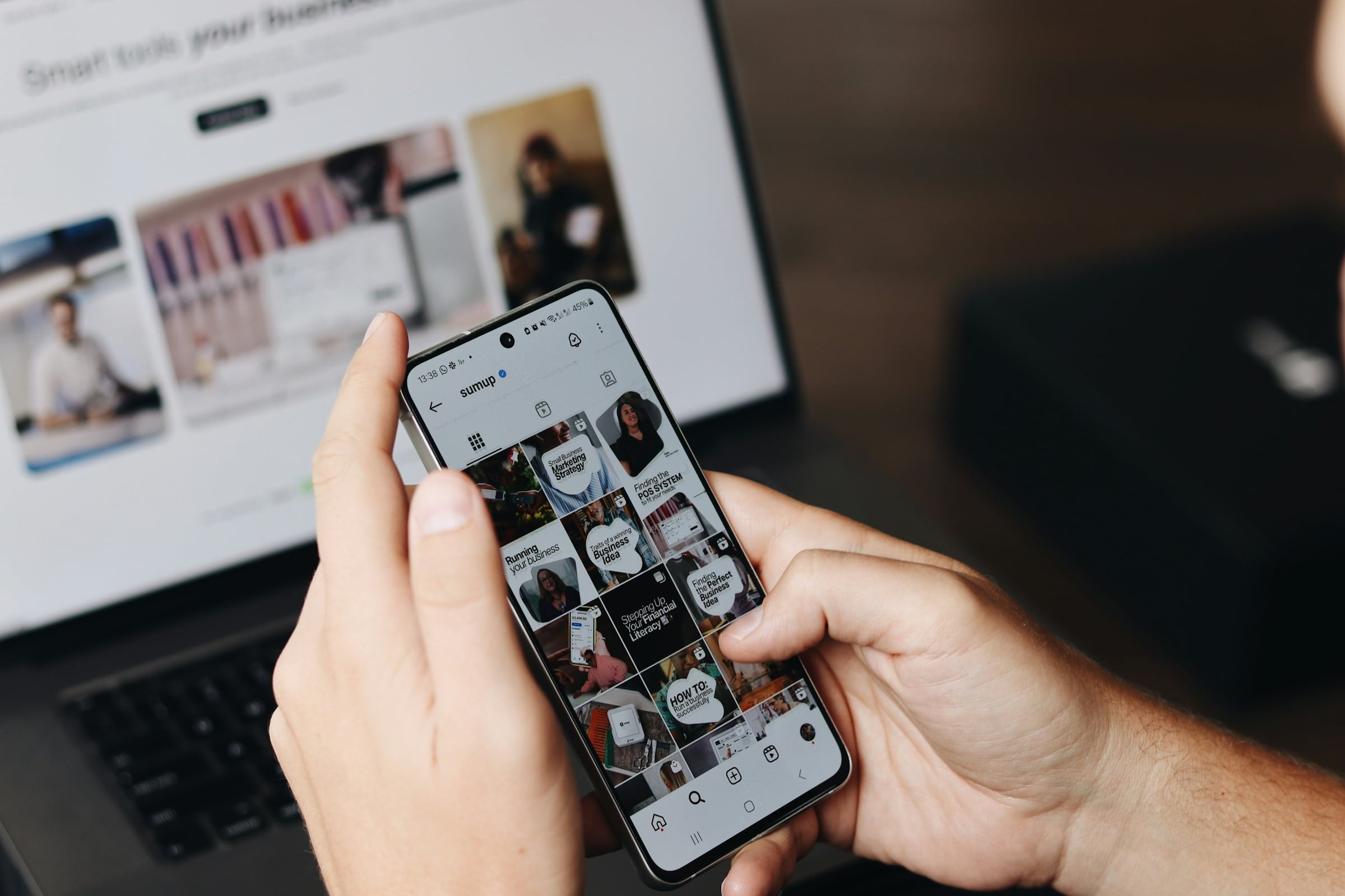 Marketer browsing a brand's social profile on a phone in front of a laptop