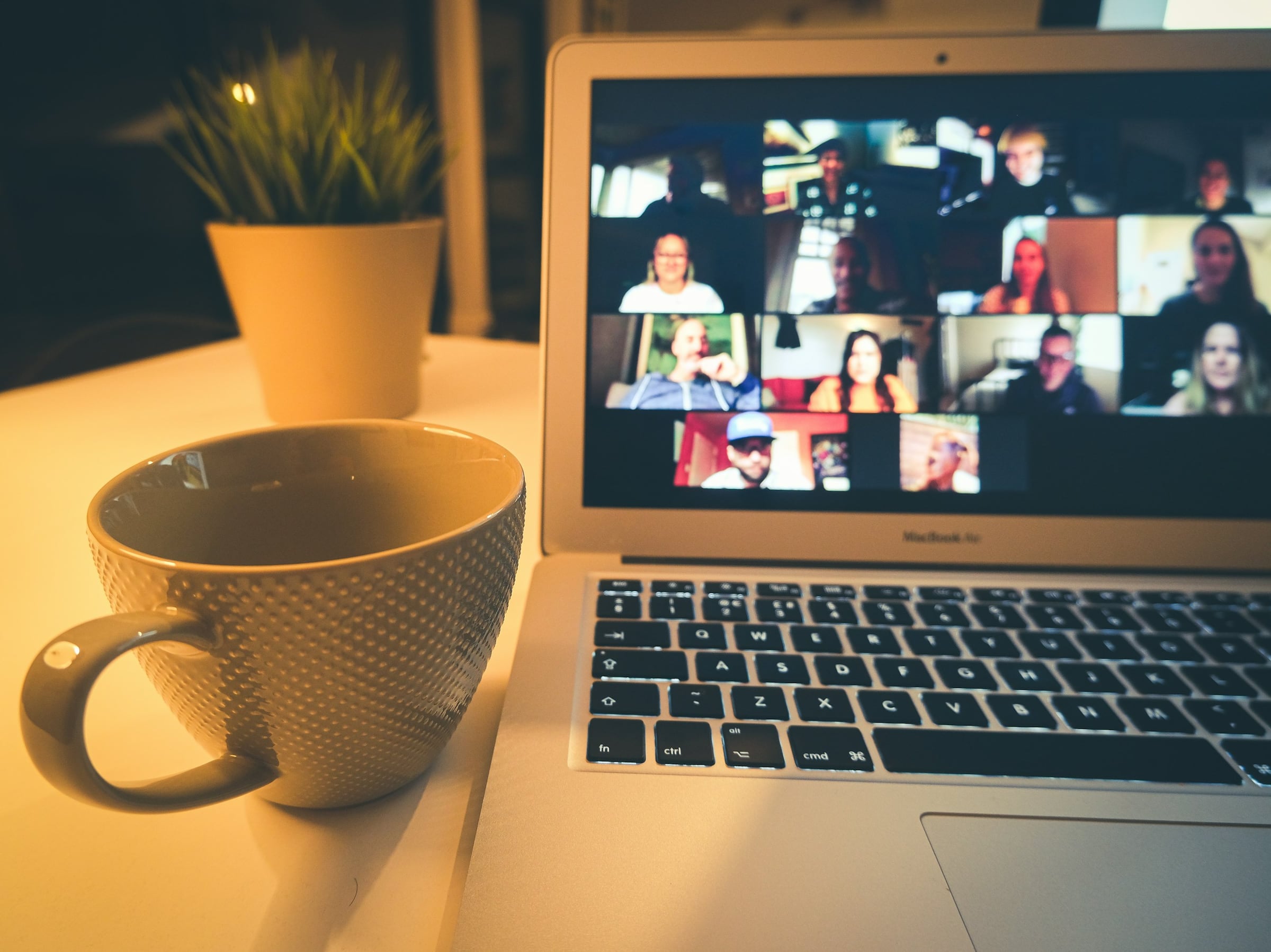 Laptop showing a group video conference next to a coffee mug
